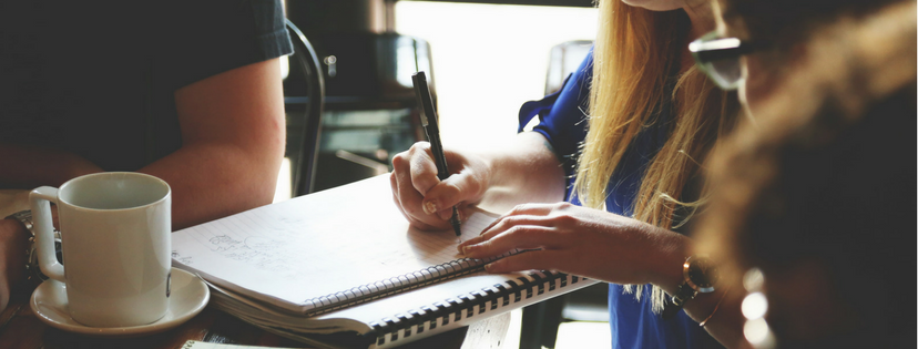 Eine Person mit Kaffeetasse, Block und Stift
